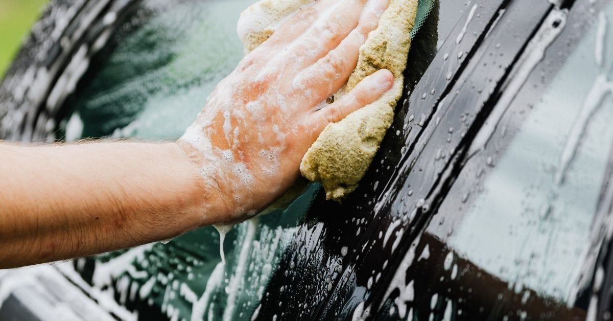 A hand washing a dark car with a soapy sponge.