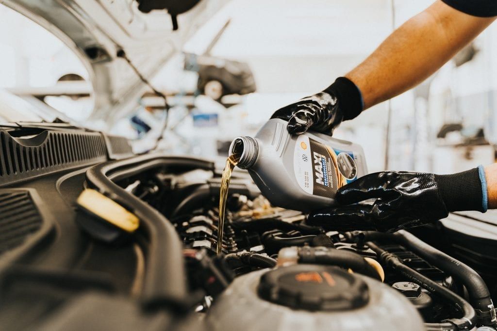 Gloved hands pouring fresh oil into a car’s engine.