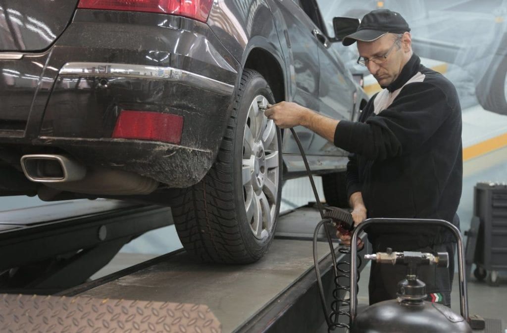 A technician checking a tire’s pressure on a car raised on a lift.