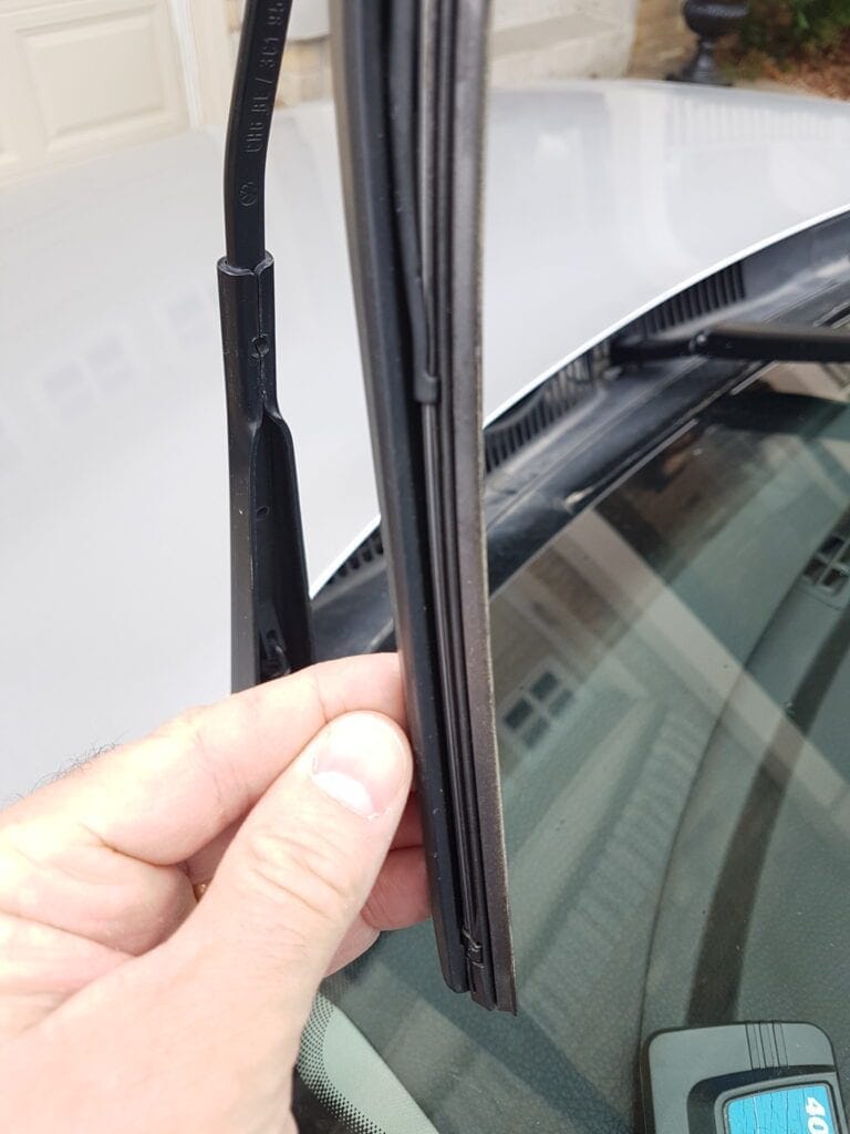 Hand holding up a windshield wiper blade to inspect its rubber edge