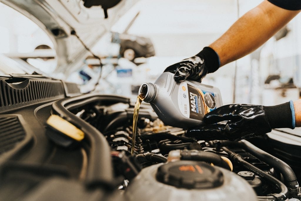 Gloved hands pouring fresh oil into a car’s engine