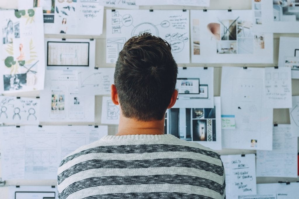 Man facing a wall covered in notes and sketches
