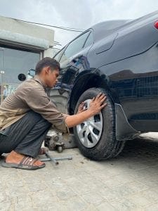 Mechanic crouched at a car’s rear wheel during a tire rotation
