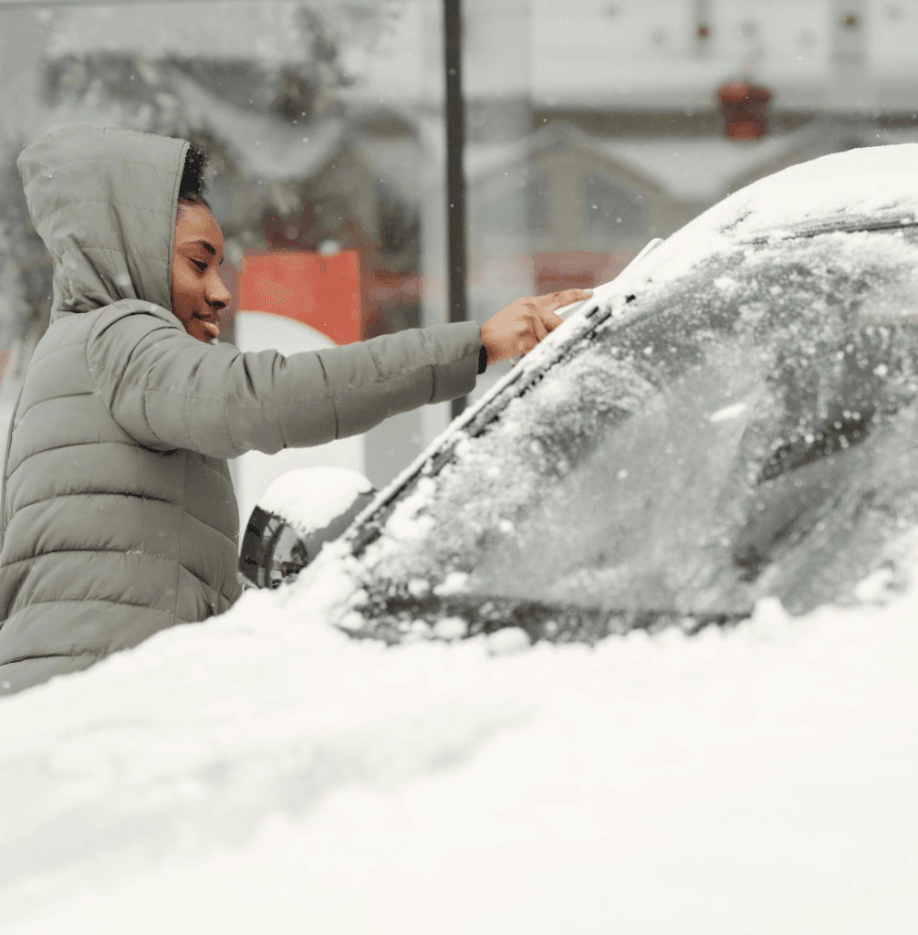 Person brushing snow off a car’s windshield