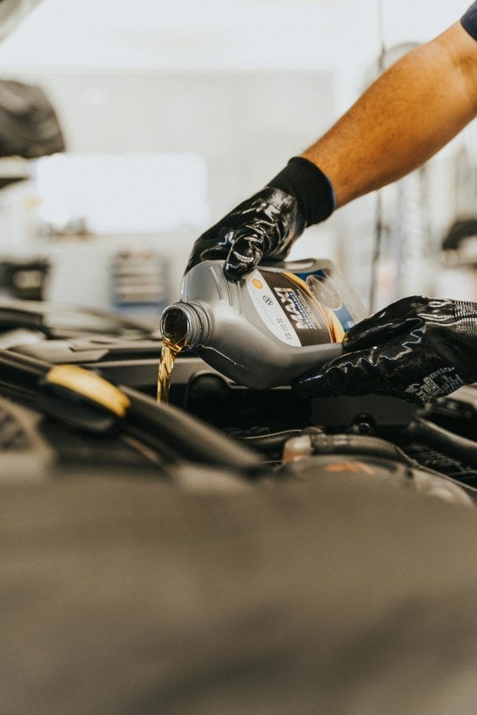 Closeup of mechanic's hands pouring a liter of fresh oil into the top of a car engine.