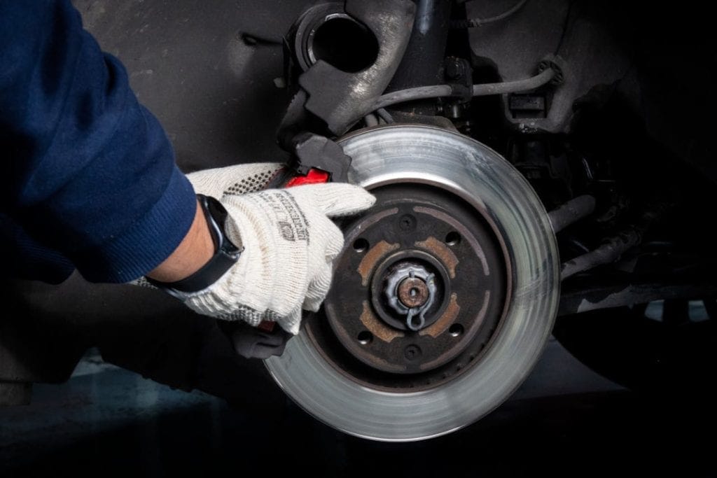 Closeup of mechanic's hands replacing a brake caliper onto a car brake rotor.