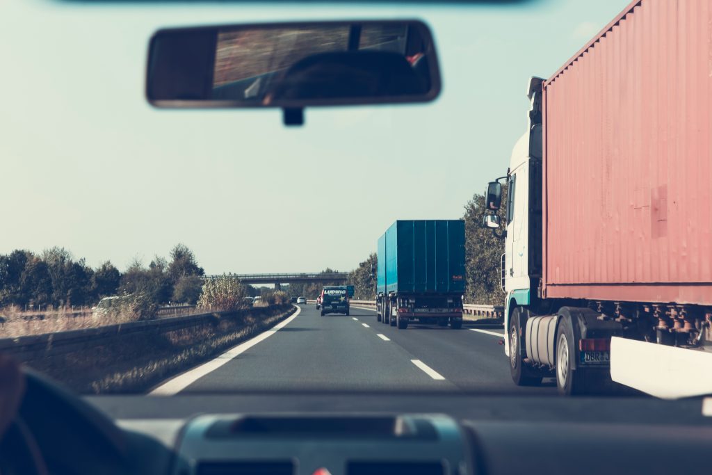 Looking out front driver's side window of a car driving while driving in the blind spot of a large truck in the right lane.