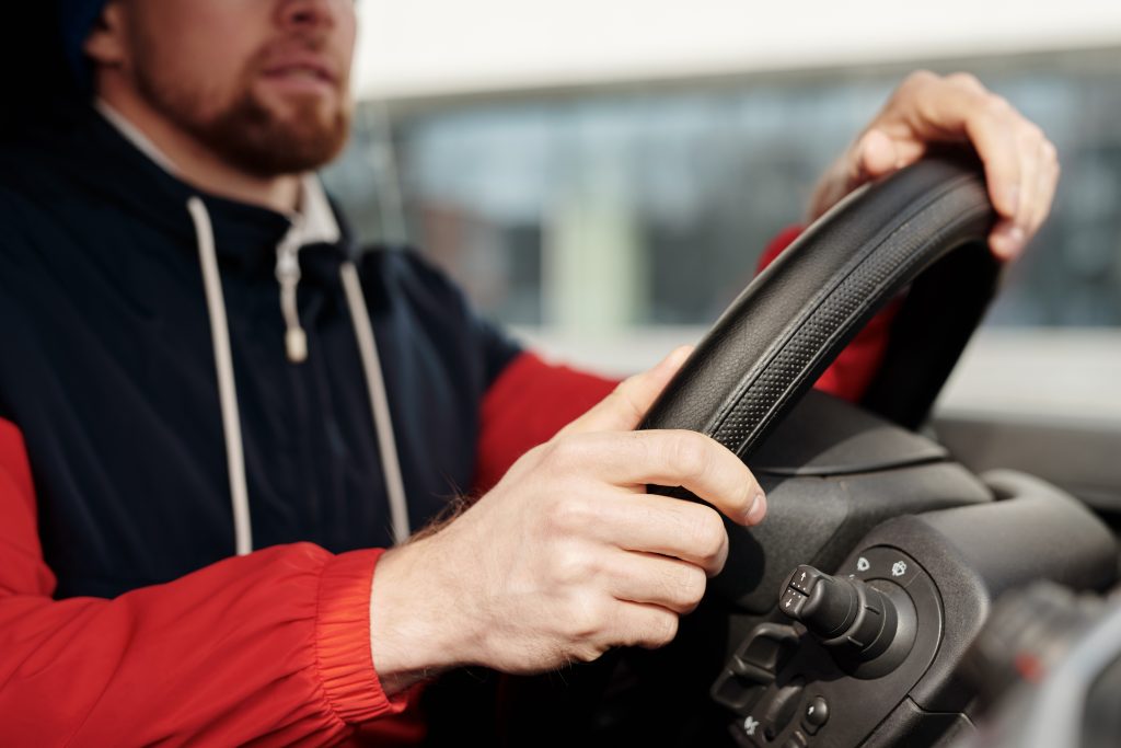 A person driving a car with both hands on the steering wheel focused on the road ahead.