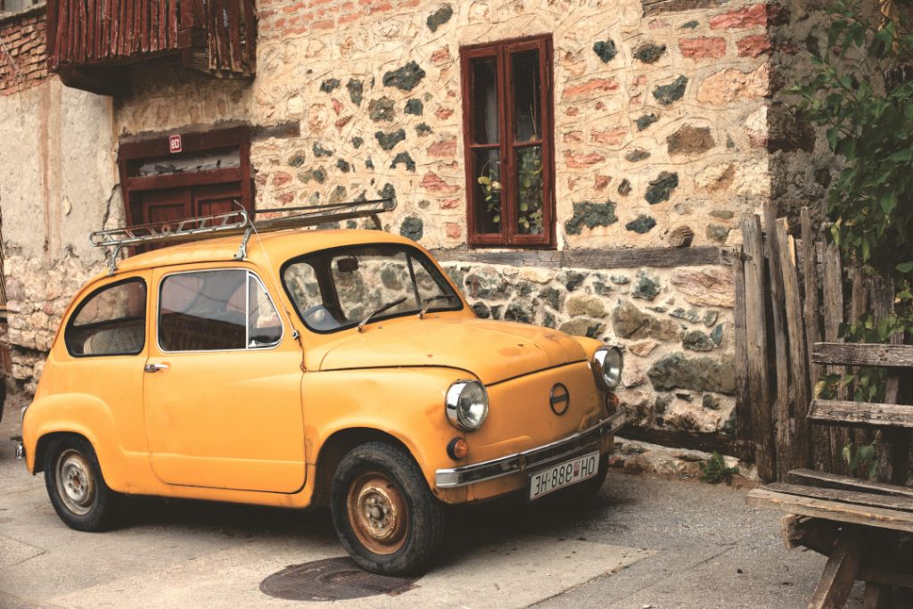 An old European car parked outside of an old stone house.