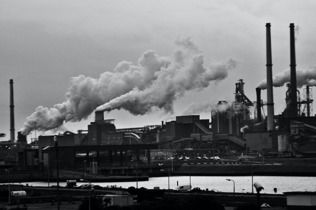 Black-and-white image of a factory with smoke coming out of smoke stacks