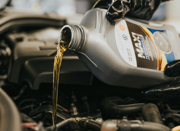 A hand pouring engine oil from oil bottle into oil tank.