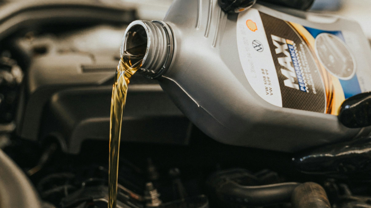 A hand pouring engine oil from oil bottle into oil tank.