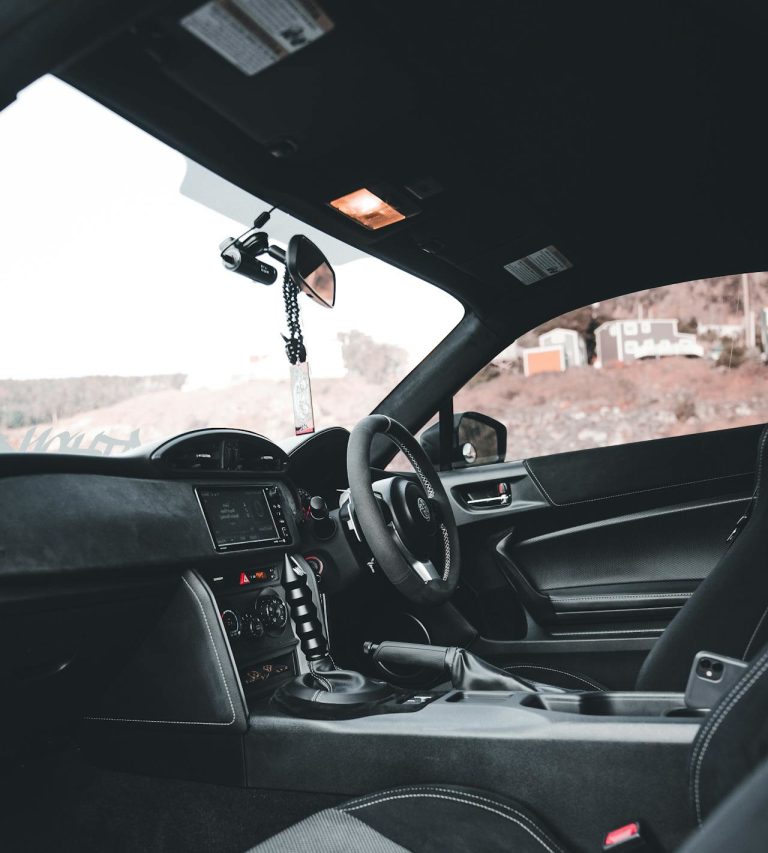 Image of inside of a car from the passenger perspective with focus on the rear view mirror and camera hanging from the top of the inside of the windscreen.
